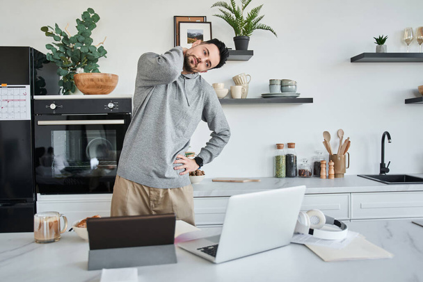 Uomo che fa un riscaldamento durante il lavoro al computer portatile mentre in piedi in cucina - Foto, immagini