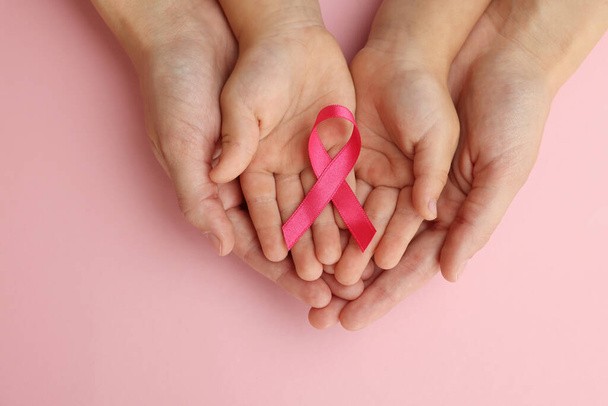 Woman and child holding pink ribbon on color background, top view. Breast cancer awareness - Zdjęcie, obraz