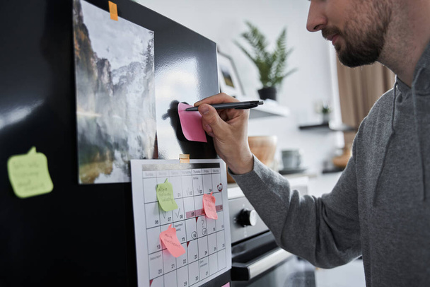 Человек, пишущий уведомления на красочной наклейке в холодильнике - Фото, изображение
