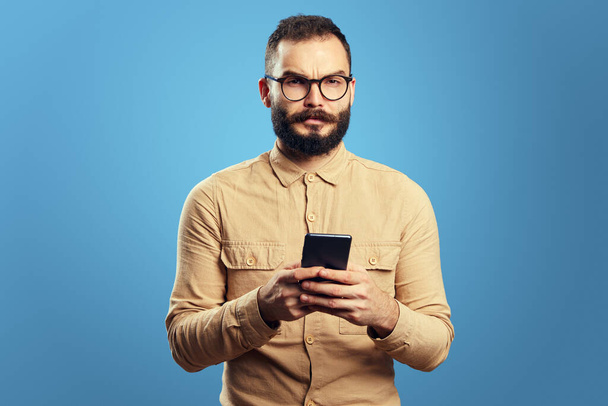 Serious adult handsome caucasian man using smartphone on blue background - Photo, Image