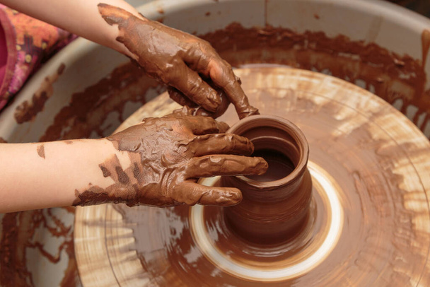 The child moulds from clay a pot on a potter's wheel. Adults help the child to work with clay. - Photo, Image