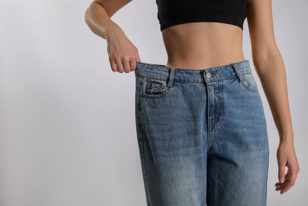 Skinny woman in oversized jeans on light background, closeup with space for text. Weight loss concept - 写真・画像