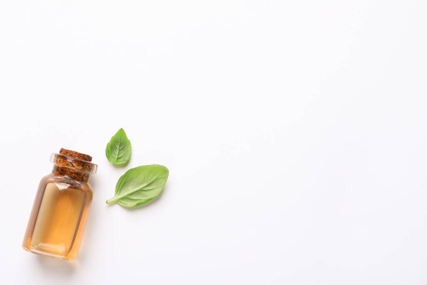 Bottle of essential basil oil and fresh leaves on white background, flat lay. Space for text - 写真・画像