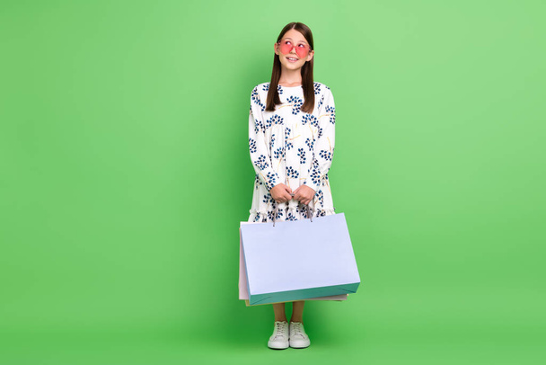 Full length photo of dreamy schoolkid look empty space hold bags dream boutique offer low price isolated over green color background - Foto, afbeelding