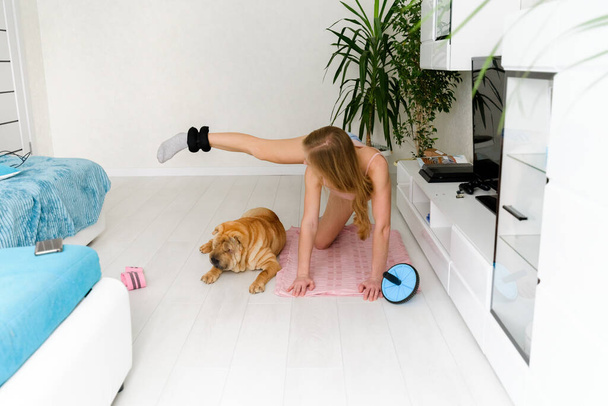 a young woman doing sports at home with her pets, a sharpey dog and a cat. self isolation taking care of yourself about the body. - Photo, image