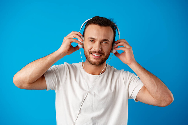 Young man listening to music with headphones on blue background. - Фото, изображение