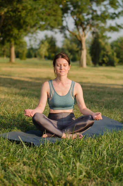 Mladá žena medituje v parku v lotosové pozici při západu slunce. Lekce jógy v přírodě - Fotografie, Obrázek