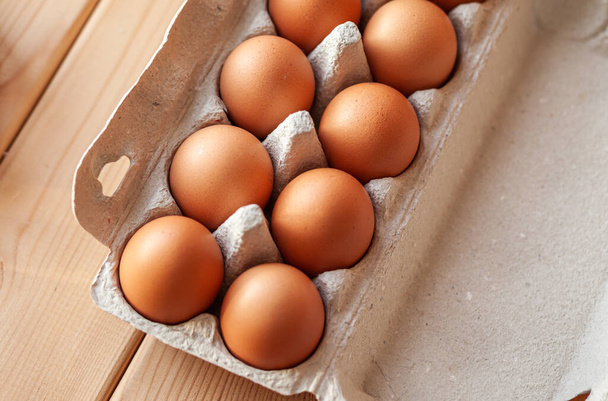 Τα καφέ αυγά κοτόπουλου είναι σε ένα χαρτόκουτο που αγοράστηκε από ένα μπακάλικο. Υγιές πρωινό. Ένα δίσκο για τη μεταφορά και την αποθήκευση εύθραυστων αυγών. Μια γυναίκα βγάζει ένα αυγό από το πακέτο με το χέρι της. - Φωτογραφία, εικόνα