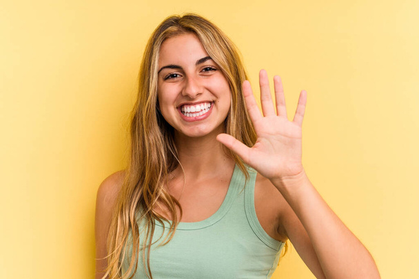 młody biały blondynka kobieta odizolowany na żółty tło uśmiech wesoły pokazując numer pięć z palce. - Zdjęcie, obraz