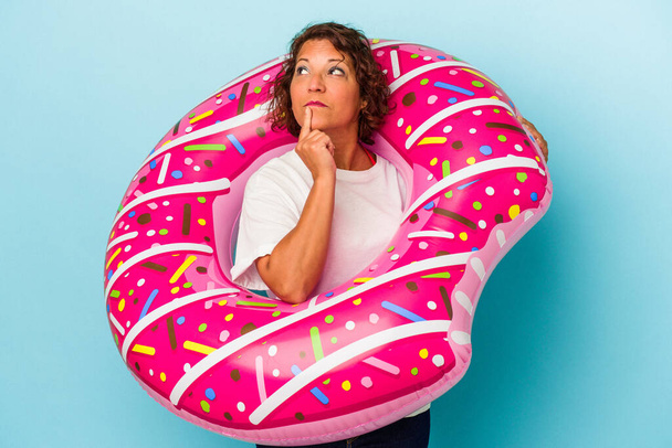 Middle age latin woman with air mattress isolated on white background looking sideways with doubtful and skeptical expression. - Photo, Image