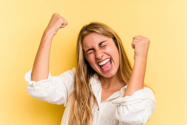 Young caucasian blonde woman isolated on yellow background  raising fist after a victory, winner concept. - Photo, Image
