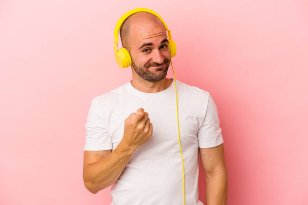 Νεαρός καυκάσιος φαλακρός άντρας που ακούει μουσική απομονωμένος σε ροζ φόντο δείχνοντας σε με το δάχτυλο σαν να σε προσκαλεί να έρθεις πιο κοντά. - Φωτογραφία, εικόνα
