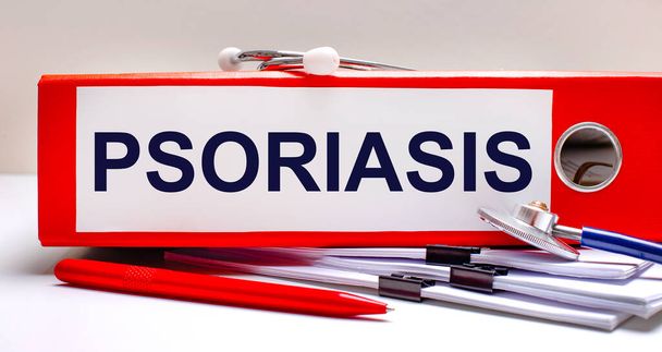 On the desktop is a stethoscope, documents, a pen, and a red file folder with the text PSORIASIS. Medical concept - Valokuva, kuva