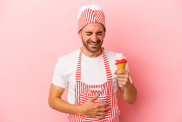 Young ice cream maker man holding ice cream isolated on pink background  laughing and having fun. - Fotografie, Obrázek