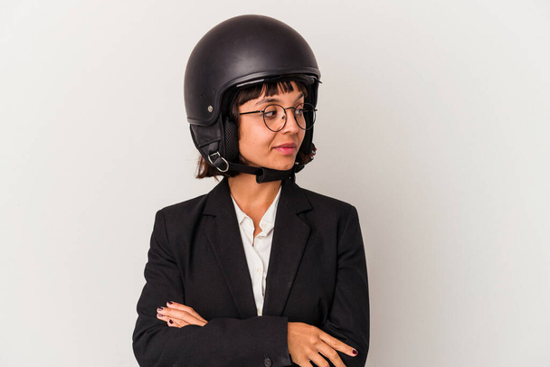 Joven mujer de negocios de raza mixta con un casco de moto aislado se ve a un lado sonriente, alegre y agradable. - Foto, imagen