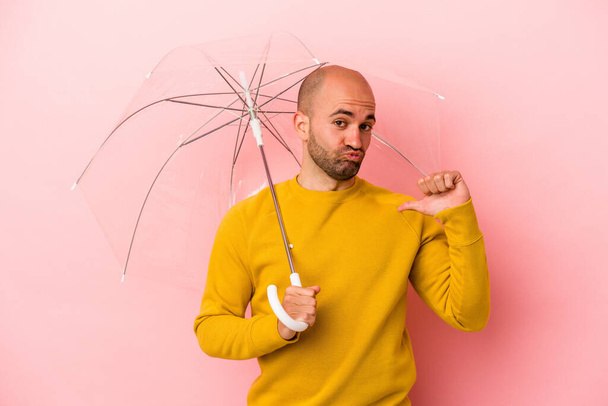 Young caucasian bald man holding umbrella isolated on pink background  feels proud and self confident, example to follow. - Photo, Image