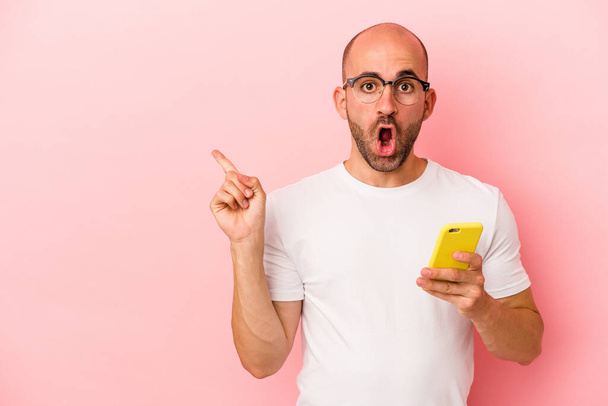 Young caucasian bald man holding mobile phone isolated on pink background  pointing to the side - Photo, Image
