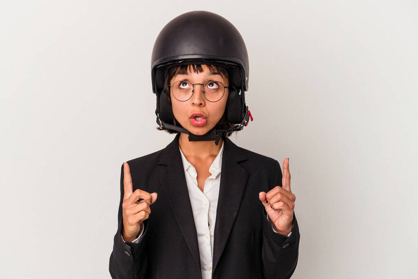Jonge gemengde ras zakenvrouw het dragen van een motorfiets helm geïsoleerd wijzen upside met geopende mond. - Foto, afbeelding