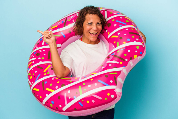 Middle age latin woman with air mattress isolated on white background smiling and pointing aside, showing something at blank space. - Foto, Imagen