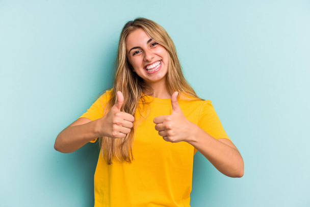 Young caucasian blonde woman isolated on blue background  smiling and raising thumb up - Foto, Imagen