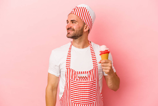 Jeune machine à crème glacée homme tenant la crème glacée isolé sur fond rose regarde de côté souriant, gai et agréable. - Photo, image