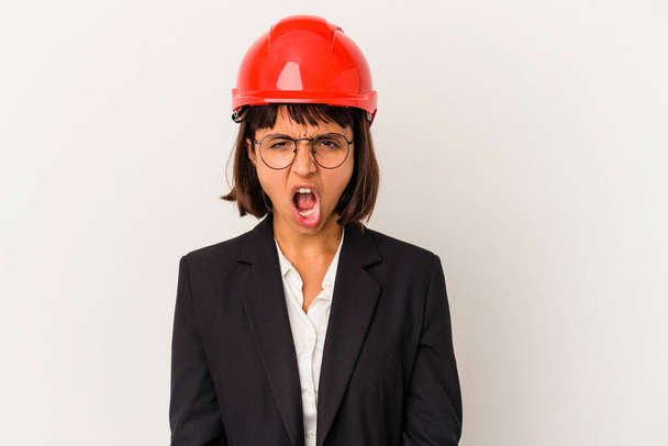 jonge architect vrouw met rode helm geïsoleerd op witte achtergrond schreeuwen zeer boos en agressief. - Foto, afbeelding