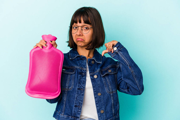 Young mixed race woman holding a hot bottle water isolated on blue background feels proud and self confident, example to follow. - Foto, afbeelding