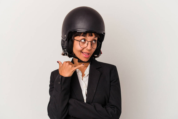 Joven mujer de negocios de raza mixta con un casco de moto aislado mostrando un gesto de llamada de teléfono móvil con los dedos. - Foto, imagen