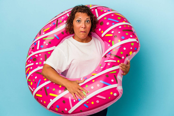 Middle age latin woman with air mattress isolated on white background shrugs shoulders and open eyes confused. - Фото, изображение