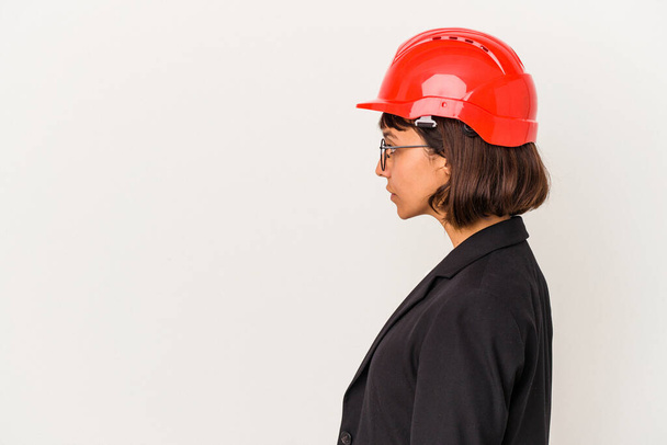 Молодая архитектор женщина с красным шлемом изолированы на белом фоне глядя влево, в сторону позировать. - Фото, изображение
