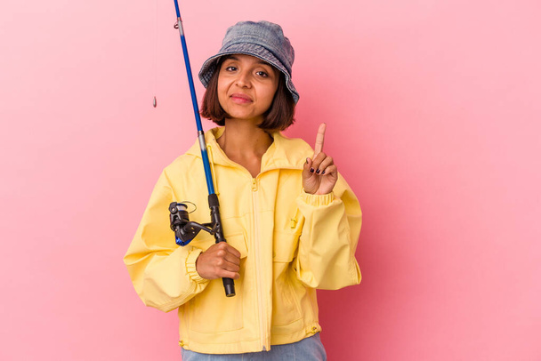 Pembe arka planda izole edilmiş balık tutma pratiği yapan genç bir ırk kadını parmaklarıyla bir numarayı gösteriyor.. - Fotoğraf, Görsel