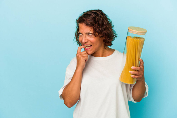 Middle age latin woman holding pasta jar isolated on blue background relaxed thinking about something looking at a copy space. - Foto, Imagen