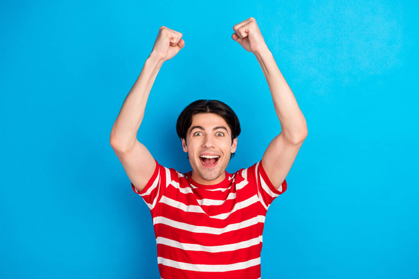 Photo of impressed shiny young guy dressed red t-shirt rising fists smiling isolated blue color background - Foto, Imagem