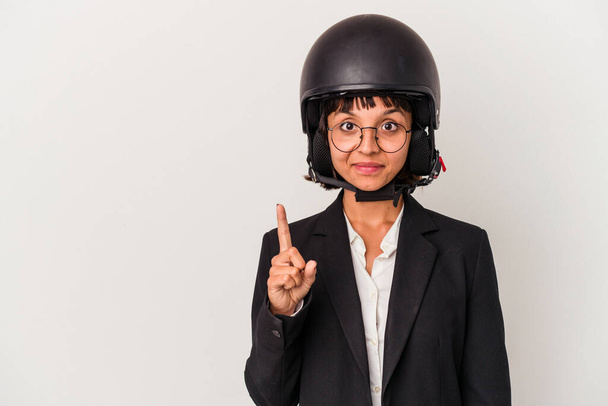 Joven mujer de negocios de raza mixta con un casco de moto aislado mostrando el número uno con el dedo. - Foto, imagen