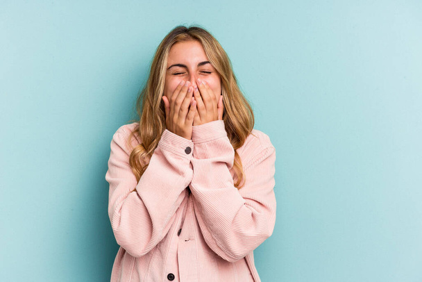 Young caucasian blonde woman isolated on blue background  laughing about something, covering mouth with hands. - 写真・画像