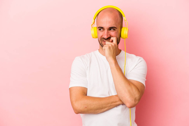 Молодий білий чоловік слухає музику ізольовано на рожевому фоні розслаблене мислення про те, що дивиться на копіювальний простір
. - Фото, зображення