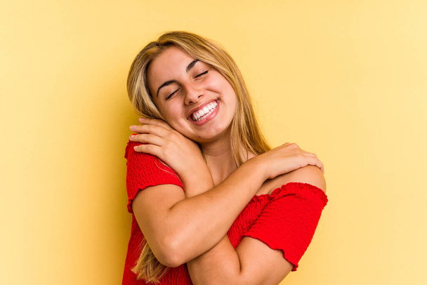 Nuori valkoihoinen blondi nainen eristetty keltainen tausta halauksia, hymyillen huoleton ja onnellinen. - Valokuva, kuva