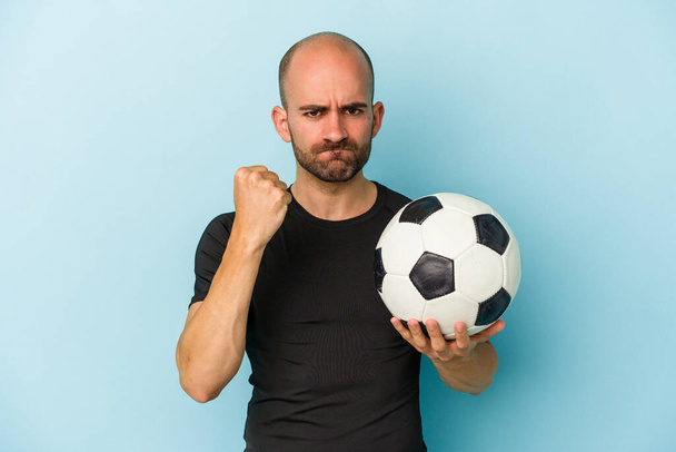 若いビジネスはげ男は、カメラに拳を示す青の背景に隔離されたサッカーをプレイ,積極的な顔の表情. - 写真・画像