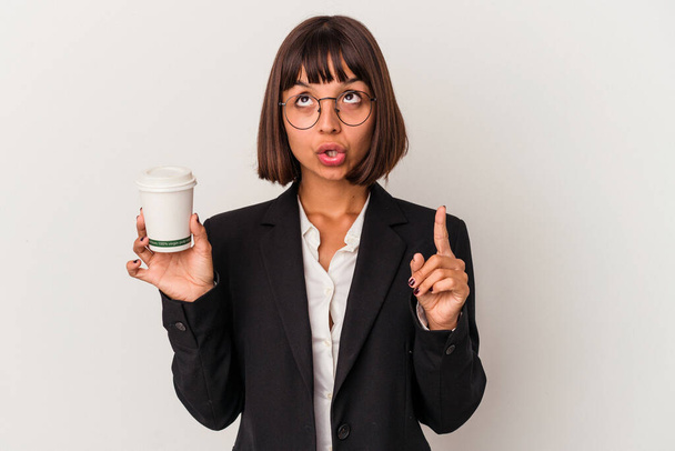 Young mixed race business woman holding a coffee isolated on white background pointing upside with opened mouth. - 写真・画像