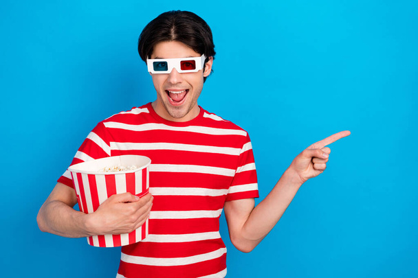 Photo of shocked cute young guy dressed red t-shirt 3d eyewear eating pop corn pointing empty space isolated blue color background - Φωτογραφία, εικόνα