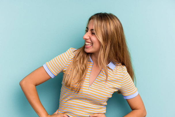 Young caucasian blonde woman isolated on blue background  laughs happily and has fun keeping hands on stomach. - Photo, Image