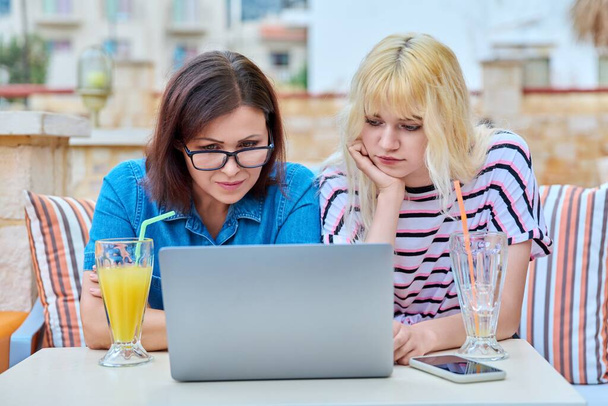 Sad upset serious mom and teenage daughter looking together into a laptop screen. - Foto, Imagen