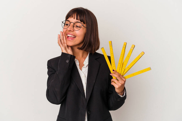 Jonge gemengde ras zakenvrouw met een maatregel tape geïsoleerd op witte achtergrond schreeuwen en houden palm in de buurt van geopende mond. - Foto, afbeelding