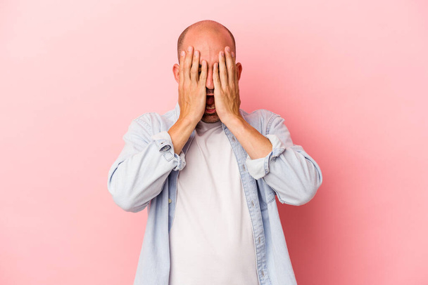 Young caucasian bald man isolated on pink background  having fun covering half of face with palm. - Foto, afbeelding