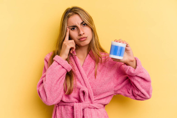 Young caucasian blonde woman holding cotton buds isolated on yellow background  pointing temple with finger, thinking, focused on a task. - Photo, Image