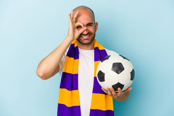 Молодий спортивний лисий чоловік в шарфі ізольований на синьому фоні, збуджений тримаючи ок жест на очах
. - Фото, зображення