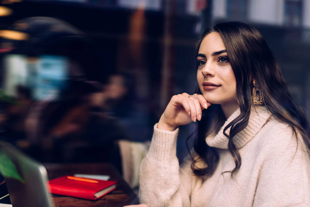 Side view of concentrated thoughtful female employee working online remotely sitting in cozy cafe using laptop looking away pondering idea for project - 写真・画像