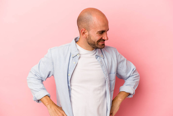 Young caucasian bald man isolated on pink background  confident keeping hands on hips. - Valokuva, kuva