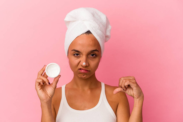 Young mixed race woman holding facial cream isolated on pink background showing a dislike gesture, thumbs down. Disagreement concept. - 写真・画像