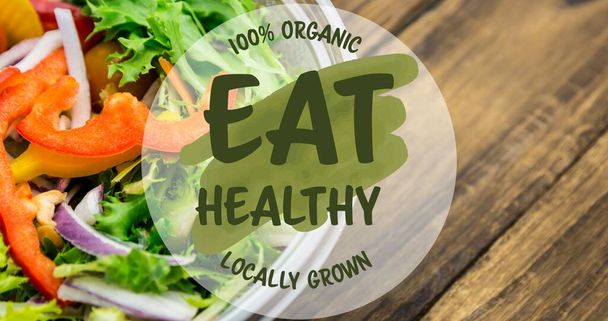 Eat healthy 100 percent organic locally grown symbol on fresh salad on table. digital composite of healthy food and sign. - Фото, зображення